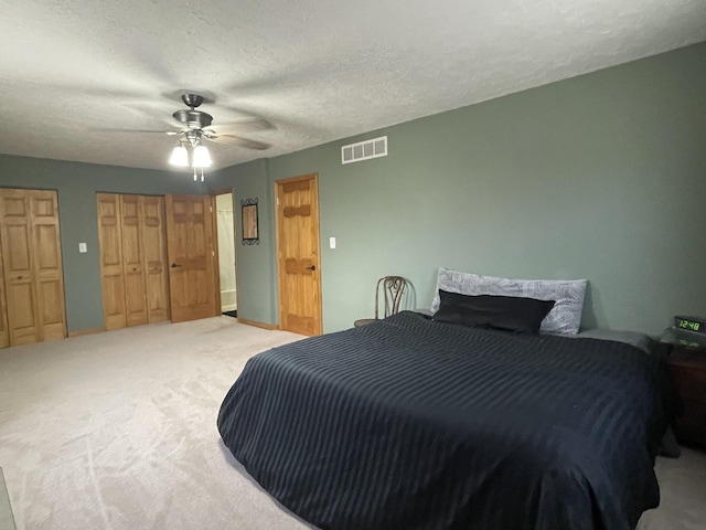 bedroom with a ceiling fan, visible vents, carpet floors, multiple closets, and a textured ceiling