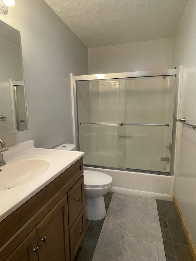 bathroom with vanity, toilet, combined bath / shower with glass door, and a textured ceiling