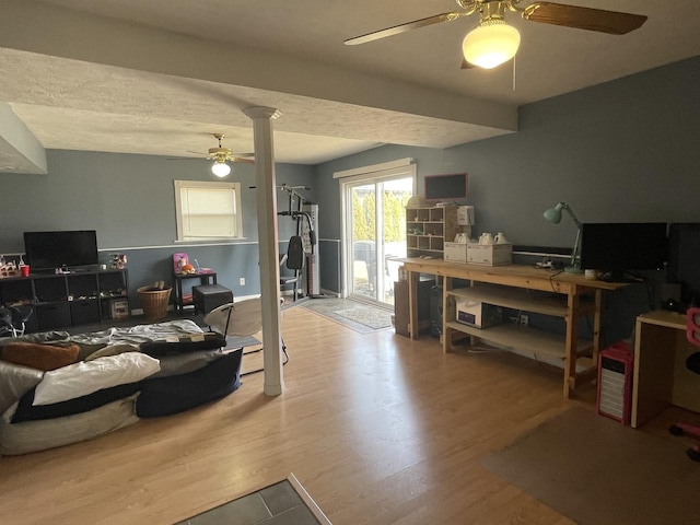 living area with decorative columns, wood finished floors, and a ceiling fan