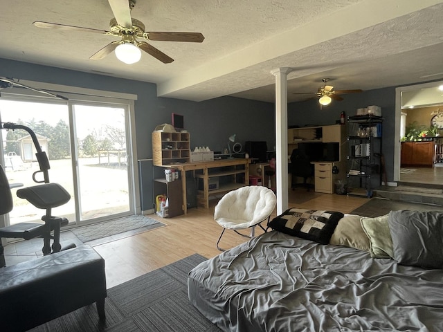 bedroom with a ceiling fan, a textured ceiling, wood finished floors, access to exterior, and ornate columns