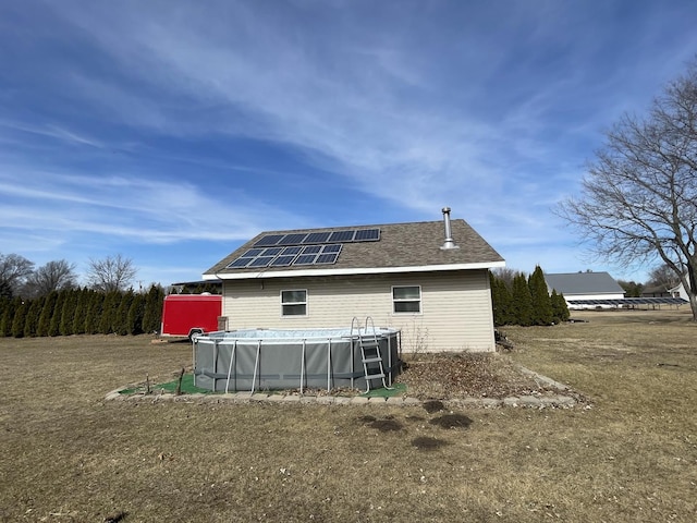 back of house featuring an outdoor pool, roof mounted solar panels, and a shingled roof