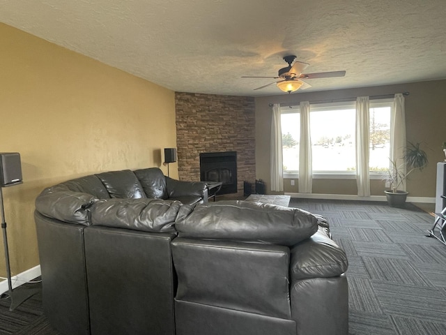 living area featuring baseboards, a fireplace, ceiling fan, a textured ceiling, and dark carpet