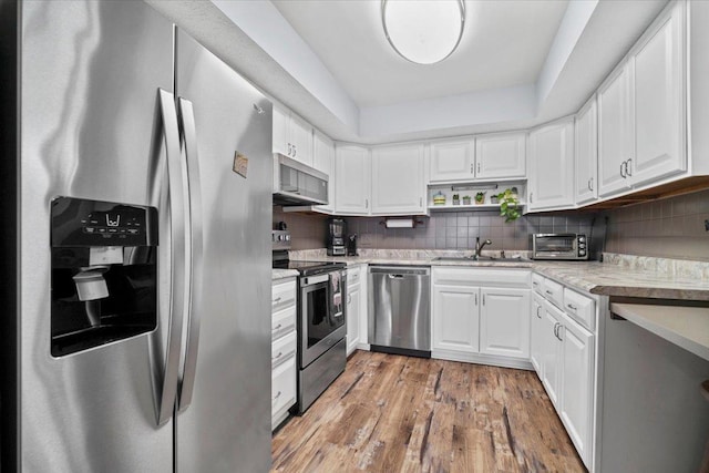 kitchen featuring stainless steel appliances, light countertops, white cabinetry, tasteful backsplash, and light wood-type flooring