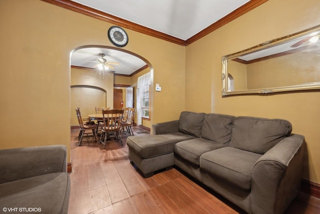 living area with arched walkways, wood finished floors, a ceiling fan, and ornamental molding