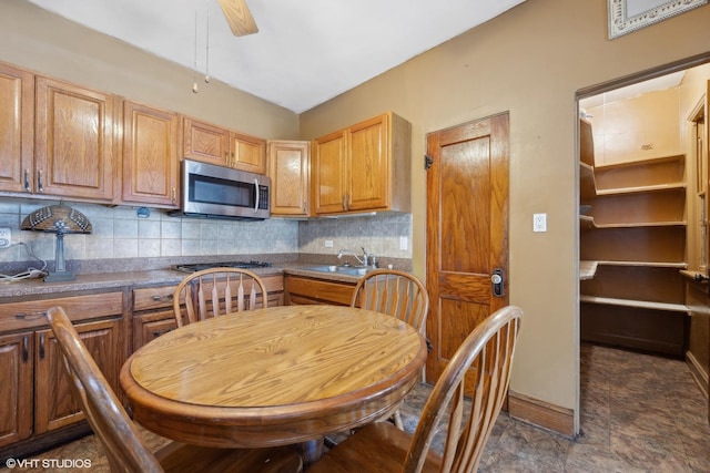 kitchen featuring tasteful backsplash, stainless steel microwave, baseboards, ceiling fan, and a sink