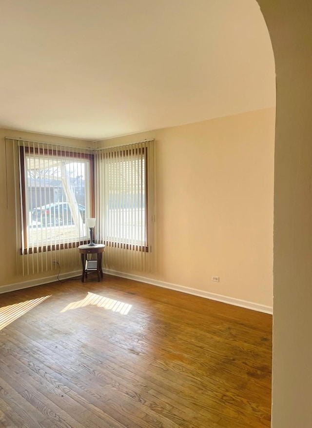 spare room with baseboards, arched walkways, and wood finished floors