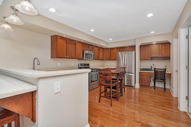 kitchen featuring light wood finished floors, light countertops, recessed lighting, brown cabinets, and appliances with stainless steel finishes