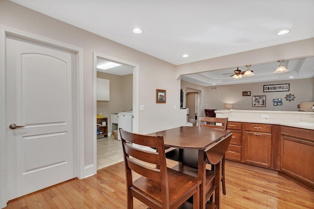 dining space with a ceiling fan, a tray ceiling, light wood-style flooring, recessed lighting, and arched walkways