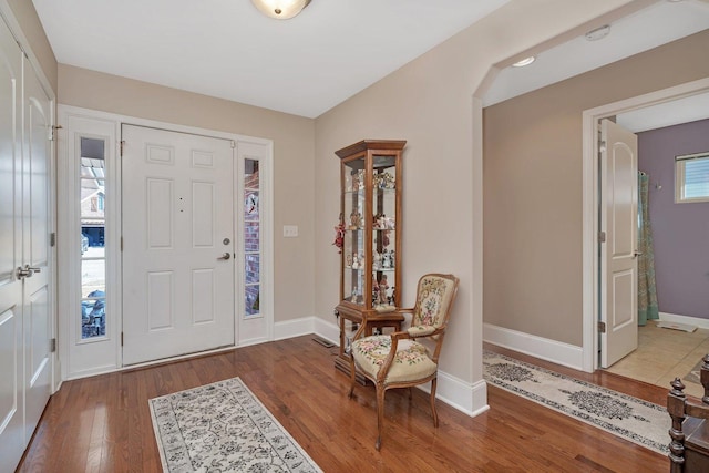 entryway featuring arched walkways, baseboards, and wood finished floors