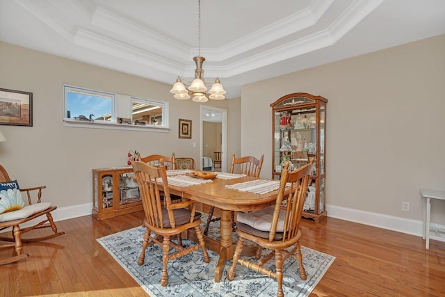 dining room featuring baseboards, a raised ceiling, light wood-style flooring, and ornamental molding