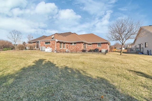 back of house with a wooden deck, brick siding, a lawn, and fence