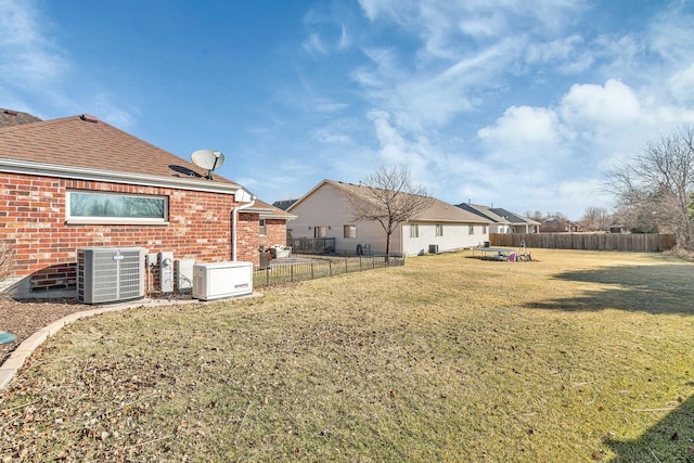 rear view of property with fence, central AC unit, roof with shingles, a lawn, and brick siding