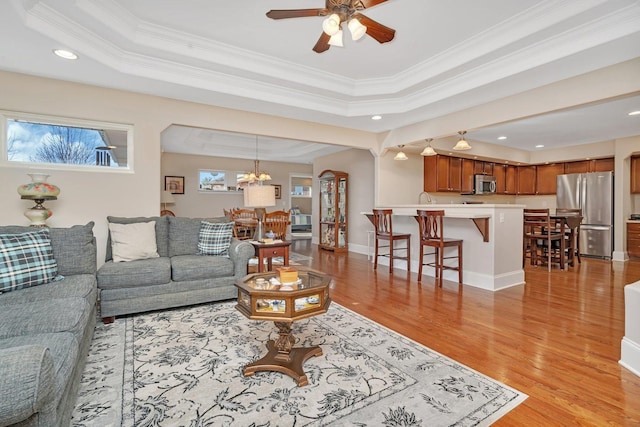 living room with a tray ceiling, crown molding, and light wood finished floors