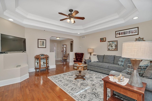 living room with a tray ceiling, arched walkways, visible vents, and wood finished floors