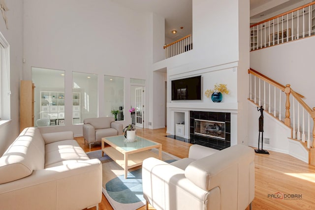 living area featuring a tiled fireplace, stairway, a high ceiling, and light wood finished floors