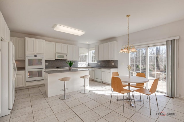 kitchen with a center island, white cabinetry, white appliances, and a breakfast bar area