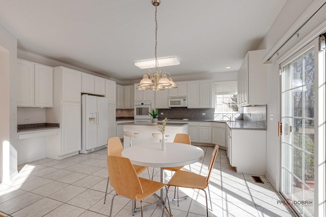 kitchen featuring white appliances, a kitchen island, light tile patterned flooring, white cabinetry, and tasteful backsplash