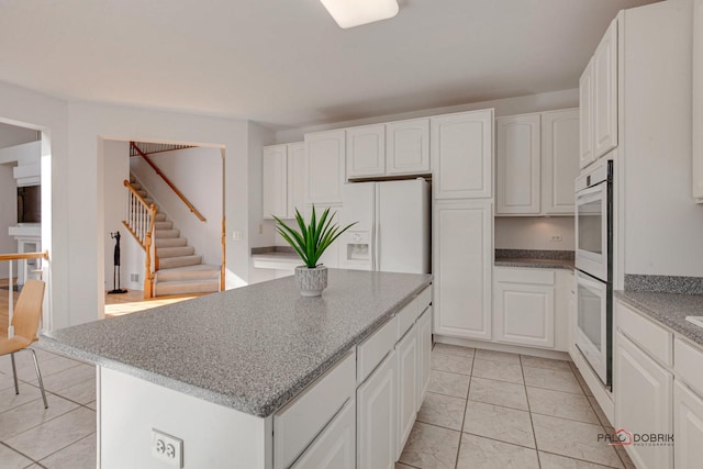 kitchen with white appliances, a kitchen island, light stone countertops, and white cabinetry