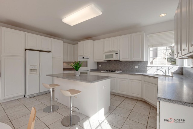 kitchen featuring white appliances, a kitchen island, a sink, white cabinetry, and tasteful backsplash