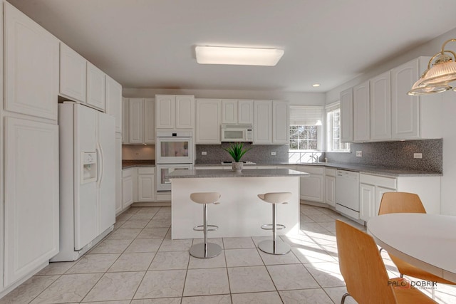 kitchen featuring tasteful backsplash, a kitchen island, a breakfast bar area, white cabinets, and white appliances