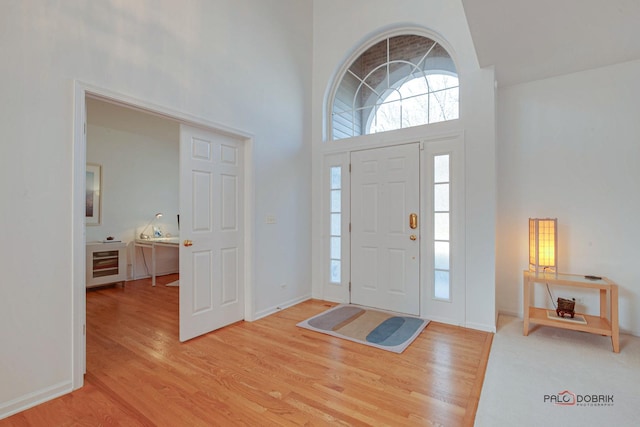 entryway featuring beverage cooler, wood finished floors, baseboards, and a towering ceiling