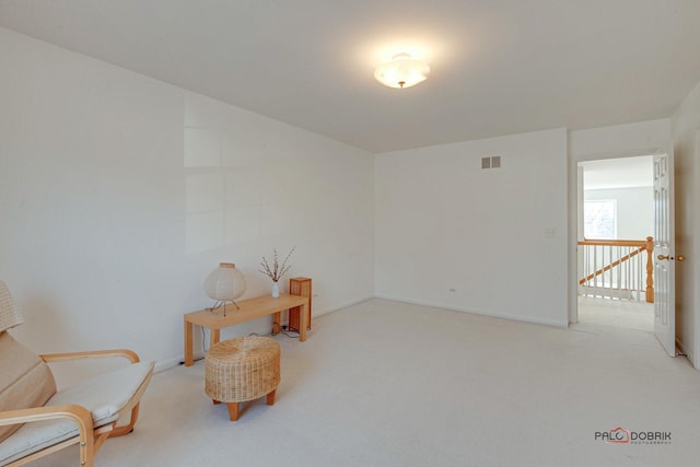 sitting room with visible vents, an upstairs landing, and light carpet