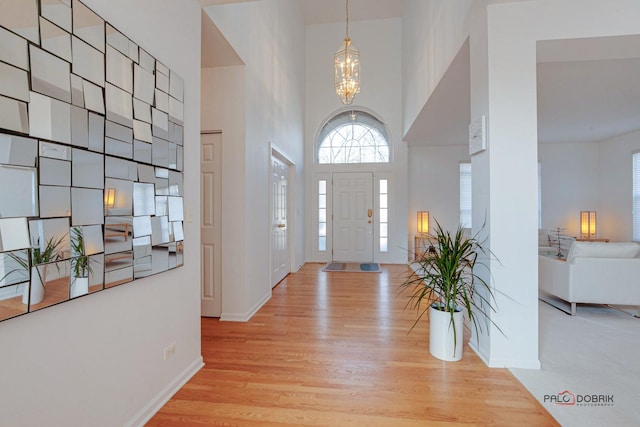 entryway featuring a towering ceiling, baseboards, an inviting chandelier, and wood finished floors