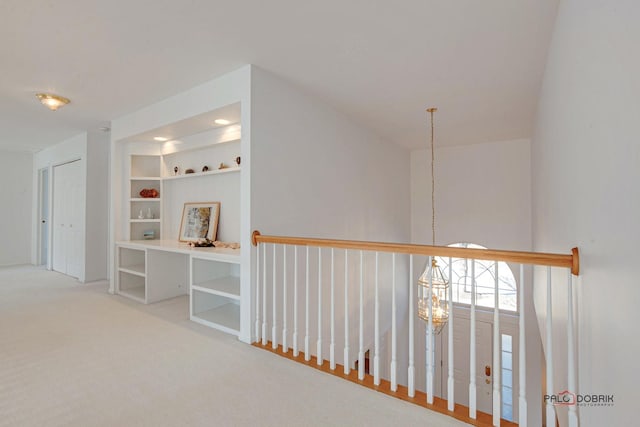 corridor featuring built in shelves, carpet, and a chandelier