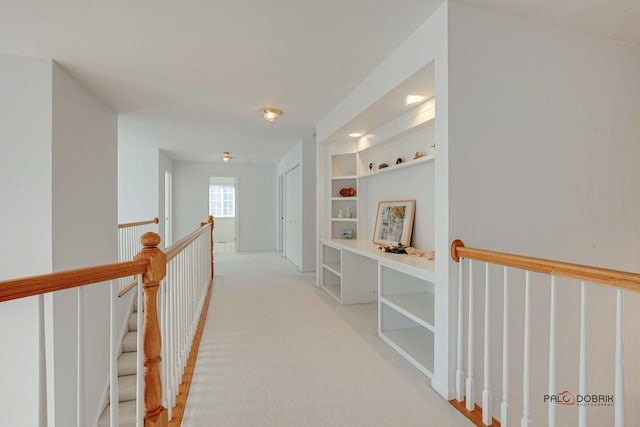 corridor with an upstairs landing, light carpet, and built in shelves