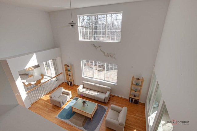 living area with ceiling fan, a healthy amount of sunlight, wood finished floors, and a towering ceiling