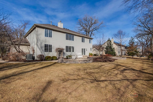 rear view of house featuring a patio, a lawn, central AC, and a chimney