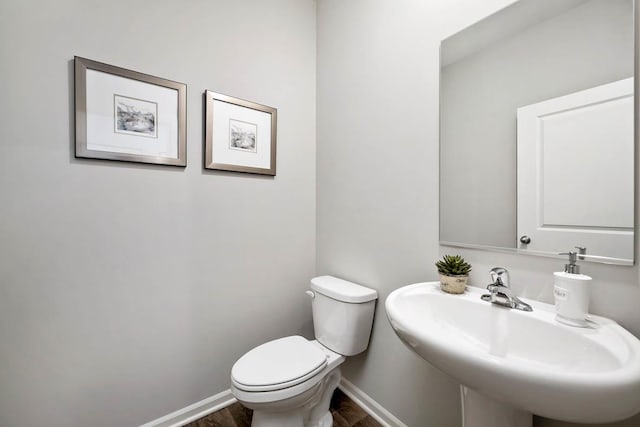 half bathroom with wood finished floors, toilet, baseboards, and a sink