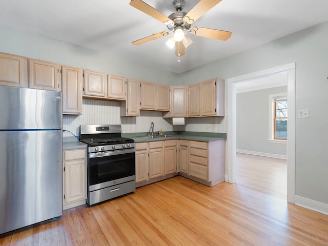 kitchen with light brown cabinets, light wood-type flooring, appliances with stainless steel finishes, a ceiling fan, and a sink