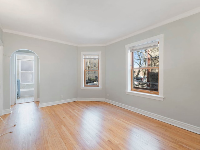 unfurnished room featuring baseboards, light wood-style floors, ornamental molding, and arched walkways