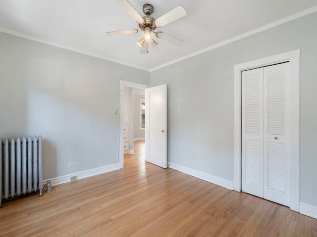 unfurnished bedroom featuring crown molding, radiator heating unit, light wood-style floors, and baseboards