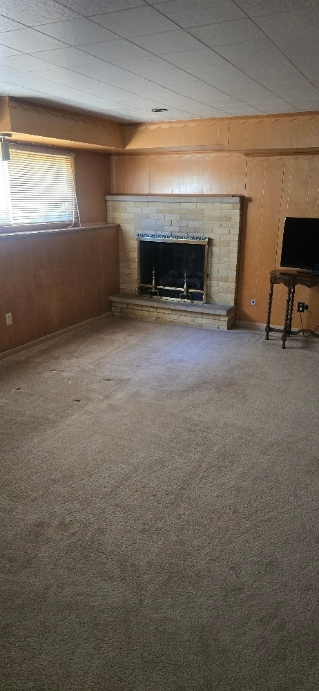 unfurnished living room featuring wooden walls, a fireplace with raised hearth, and carpet floors