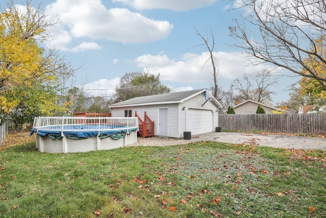 rear view of house featuring a lawn, a garage, fence, an outdoor structure, and a fenced in pool