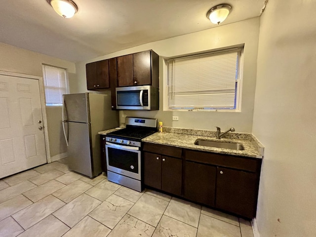 kitchen with baseboards, a sink, light stone counters, dark brown cabinets, and appliances with stainless steel finishes
