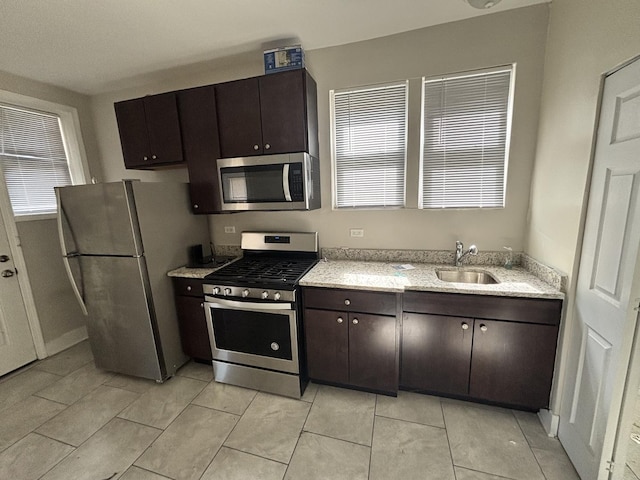 kitchen featuring a sink, stainless steel appliances, light stone countertops, and dark brown cabinetry