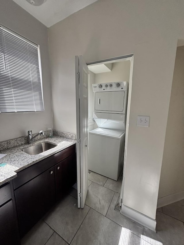 laundry room featuring baseboards, stacked washer and dryer, a sink, light tile patterned flooring, and laundry area