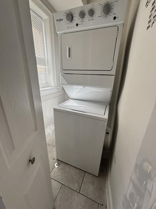 washroom with stacked washer / dryer, light tile patterned floors, and laundry area