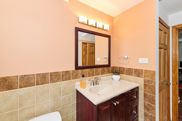 half bathroom with vanity, tile walls, toilet, and wainscoting