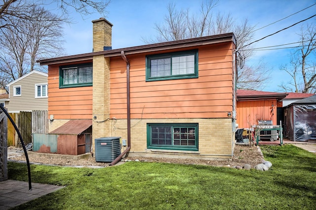 rear view of property featuring a lawn, fence, brick siding, central AC unit, and a chimney