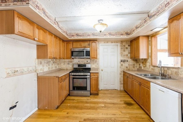 kitchen featuring backsplash, light countertops, light wood-style floors, stainless steel appliances, and a sink