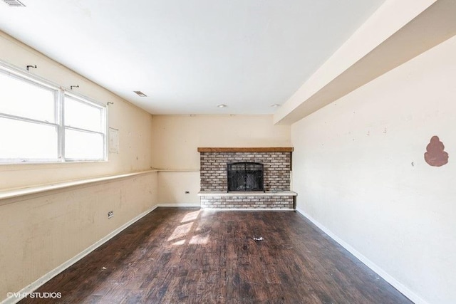 unfurnished living room with visible vents, baseboards, a brick fireplace, and wood finished floors