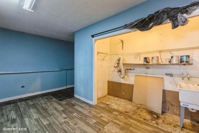 clothes washing area featuring a sink, baseboards, wood finished floors, and laundry area