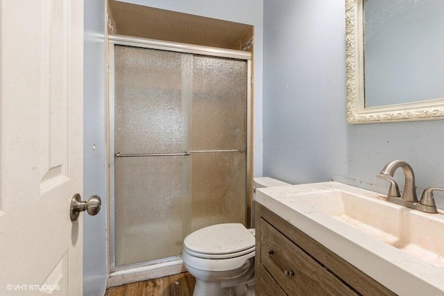 bathroom featuring vanity, toilet, wood finished floors, and a stall shower