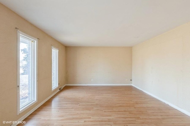 empty room with baseboards, light wood-style floors, and a healthy amount of sunlight