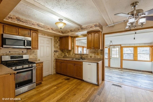 kitchen with light wood-style flooring, appliances with stainless steel finishes, brown cabinets, and a sink