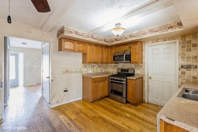 kitchen with beam ceiling, light wood finished floors, stainless steel appliances, brown cabinetry, and light countertops